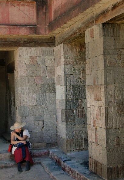 Woman in Mexican dress with hat sits in the shade of the carved pillars of the Pyramid of the Moon