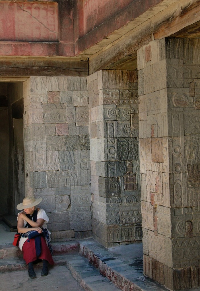 Woman in Mexican dress with hat sits in the shade of the carved pillars of the Pyramid of the Moon