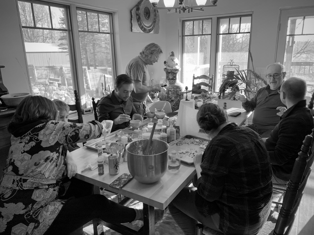 Family is gathered around the table helping decorate cookies for the holidays.