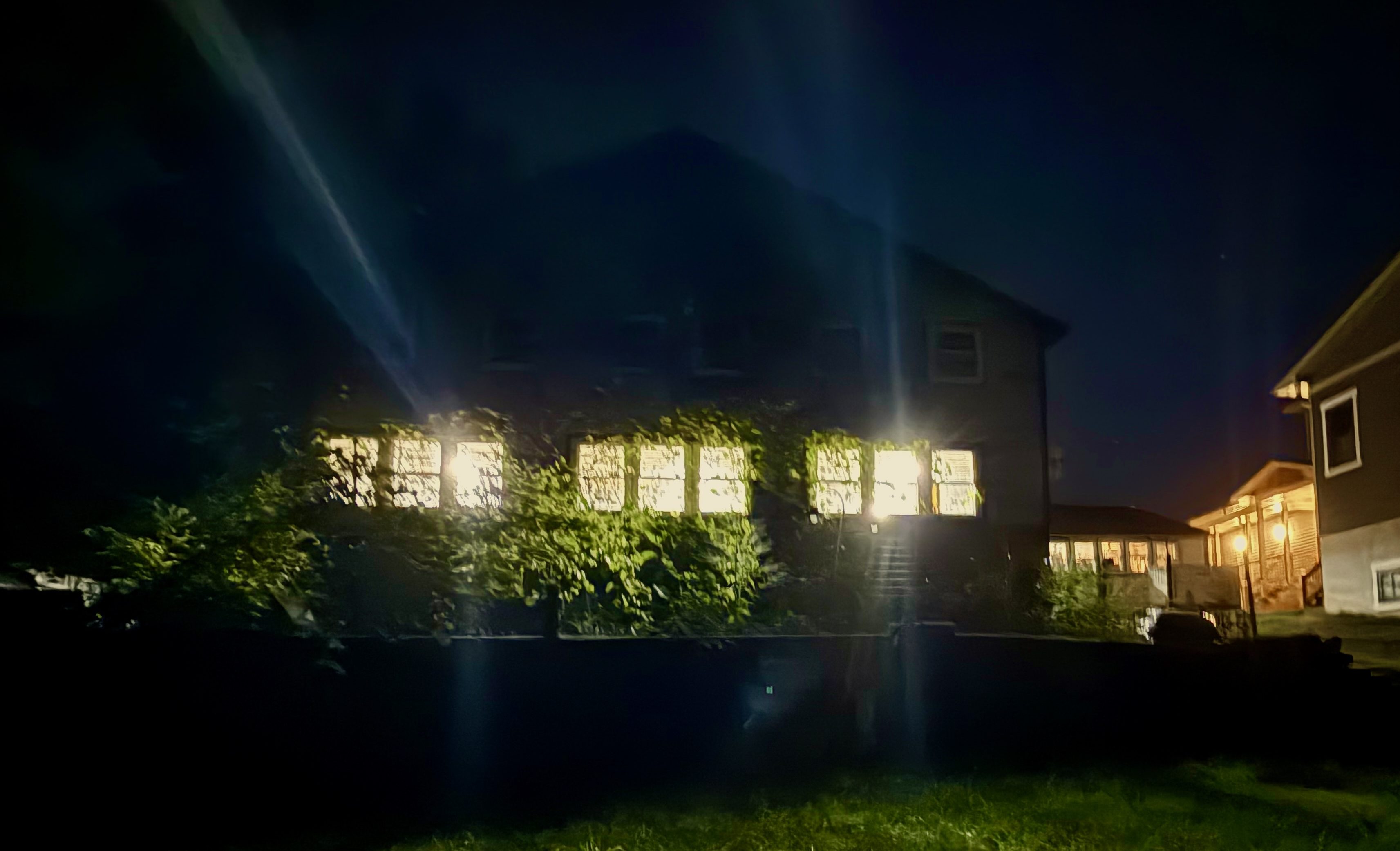 The image shows an old building at night with light streaming through windows covered by grapevines. It is the place where the author finds solace and magic in 